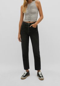 Top senza maniche, aderente, di colore grigio chiaro con texture arricciata; jeans in denim neri a vita alta; sneakers casual con dettagli in nero, grigio e marrone.