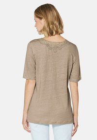 Beige Kurzarm-T-Shirt mit rundem Ausschnitt, verziert mit aufwendigen Spitze-Details auf der Rückseite, verfügt über eine weiche Textur und einen lässigen Schnitt.