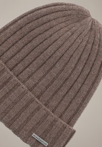 Brązowa czapka z prążkowanej dzianiny, wykonana z teksturowanej włóczki. Posiada złożony brzeg i małą metkę z nazwą marki z boku.