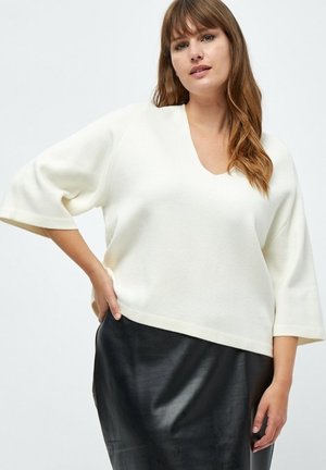 White, oversized sweater with a V-neck and wide sleeves, paired with a black leather skirt, featuring a smooth texture and minimal design.
