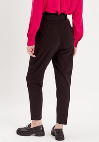 Schwarze taillierte Hosen mit schmaler Passform, knöchellang und mit Seitentaschen, kombiniert mit einer leuchtend rosa Bluse mit langen Ärmeln und schwarzen Slippern.