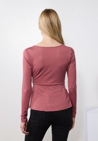 Langermet topp i mauve, laget av mykt stoff, med innsvingt midje og rund hals, kombinert med mørke jeans. Jevn tekstur, enkel design.