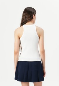 Weißes geripptes Tanktop mit taillierter Passform und rundem Ausschnitt, kombiniert mit einem marineblauen Faltenrock. Fokus auf Textur und Farbkontrast.