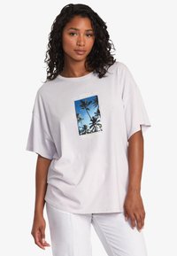 Jasnofioletowy, oversize t-shirt z niebieską grafiką palmy, otoczon�ą napisem. Krótkie rękawy i miękka, gładka faktura materiału.