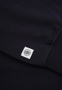 Navy sweatshirt fabric with ribbed cuffs. Features a stitched white label with "HONESTY RULES" text and circular design on the side.