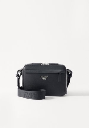 Black rectangular crossbody bag with silver logo emblem, zip closure, front pocket, and wide shoulder strap embossed with brand name.