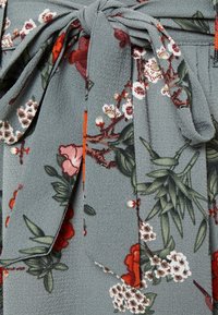 Ceinture en tissu floral en matériau gris doux et texturé, ornée de fleurs rouges, roses et blanches avec des feuilles vertes et des détails subtils.