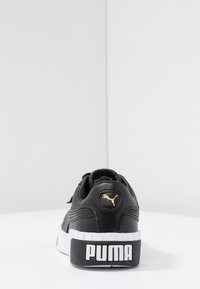 Schwarze Ledersneaker mit strukturierter Oberfläche, weißer Sohle und markantem PUMA-Logo. Goldakzent an der Ferse. Klassisches Schnürdesign.