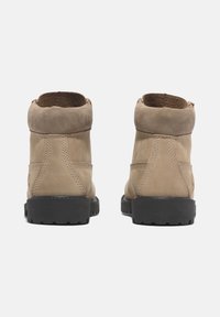 Botas de tobillo de ante marrón con un interior suave, tacón bajo y suela de goma negra texturizada. Presentan una costura simple y un diseño redondeado.