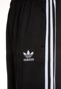 Svarta träningsbyxor med vita sidostripes. Har en mjuk textur, elastisk midja och broderad Adidas-logotyp på nedersta benet.