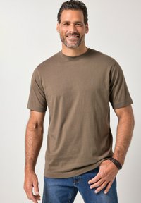 Bruine T-shirt met korte mouwen en ronde hals, gemaakt van zacht materiaal, met een subtiel logo. Draagt blauwe spijkerbroek en heeft een ontspannen pasvorm.