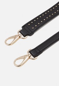 Svart lädersnodd med guldnitar, med metallspännen i båda ändar. Slät yta med förstärkt sömnad längs kanterna.