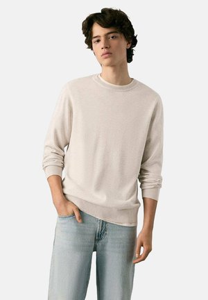 Beiger Rundhalspullover mit gerippten Bündchen und Saum, aus einem weichen Stoff, kombiniert mit hellblauen Jeans mit weitem Schnitt.