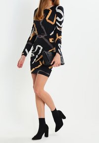Czarna sukienka bodycon z długimi rękawami i abstrakcyjnymi wzorami geometrycznymi w kolorze pomarańczowym i białym. W zestawie czarna torebka kopertówka i botki.
