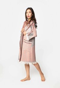 Dlhý rúch v ružovej a šedej farbe s textúrovaným vzorom, s strapcovými lemami a kapucňou. Obsahuje bočné vrecká a otvorený predný dizajn.