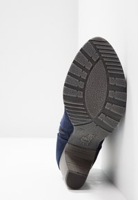 Marineblauwe suède schoen met een gestructureerde rubberen zool, voorzien van een middelhoge blokhak en een ritssluiting aan de zijkant voor gemakkelijk aan- en uitrekken. De zolen hebben een patroon van profiel.