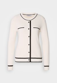 Cardigan en tricot blanc avec des bordures noires, des boutons à l'avant et deux poches poitrine avec des lignes et des points contrastants. Texture douce, manches longues.