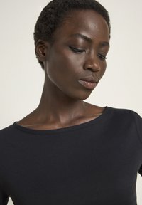 Schwarzes, figurnahes Langarmshirt aus weichem Material mit weitem Rundhalsausschnitt und subtilen Nähten, die die strukturierte Oberfläche betonen.