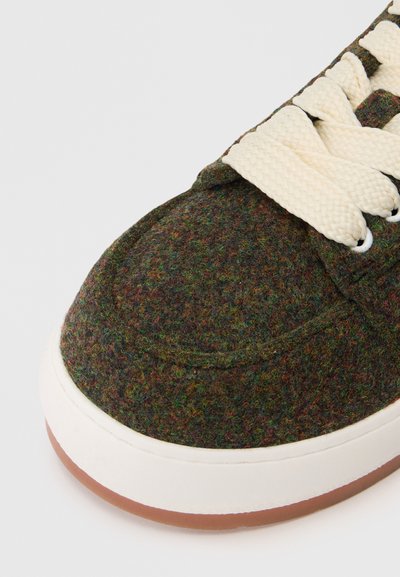 Κοντινή λήψη ενός αθλητικού παπουτσιού με σκοτεινό πολύχρωμο ύφασμα στο πάνω μέρο�ς, λευκές χοντρές κορδόνες, λευκή ενδιάμεση σόλα και ανοιχτό καφέ καουτσούκ στη σόλα.