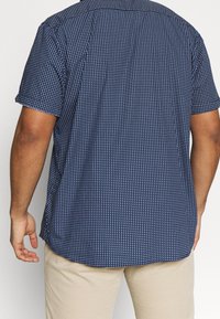 Korte mouwen overhemd in marineblauw met een wit geometrisch patroon. Voorzien van een button-down kraag en een comfortabele pasvorm. Zachte katoenstof.