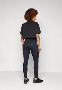 T-shirt nera corta con maniche corte, abbinata a leggings neri. Entrambi i capi presentano una superficie liscia. Le scarpe da ginnastica nere completano l'outfit.