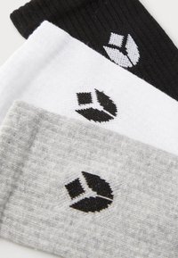 Tres pares de calcetines de tripulación en negro, blanco y gris. Cada uno tiene un diseño texturizado y presenta un logotipo negro distintivo.