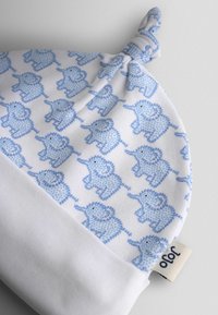 Biela detská čiapka s modrým vzorom slona, s uzlom na vrchu a preloženým lemom s značkovou nášivkou.