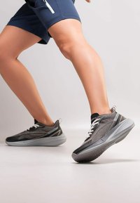 Czarne i szare buty sportowe z siateczkowej cholewki, białymi sznurówkami i teksturowaną gumową podeszwą, zaprojektowane dla komfortu i wsparcia podczas ruchu.