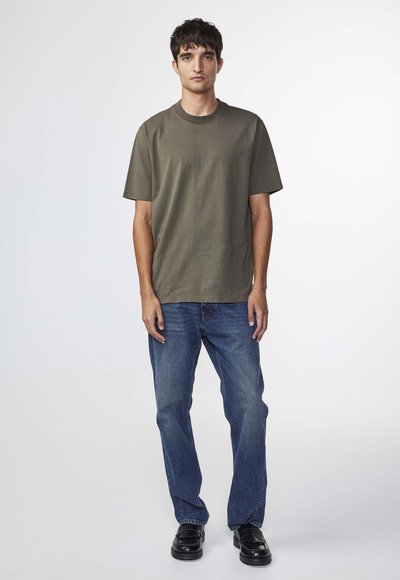 Olivengrøn t-shirt med korte ærmer, afslappet pasform, parret med blå denimjeans og sorte sko. T-shirten har et enkelt rundhalset design.