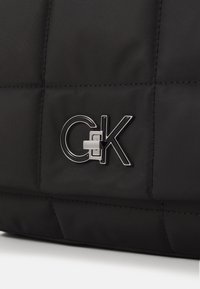 Černá prošívaná taška vyrobená z odolného nylonu, s výrazným kovovým logem C&K, hladkým povrchem a detailním prošíváním.