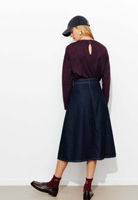 Haut à manches longues violet foncé avec un détail en clé de dos, associé à une jupe en denim foncé jusqu'aux genoux et des mocassins marron, accentué par des chaussettes rouges.