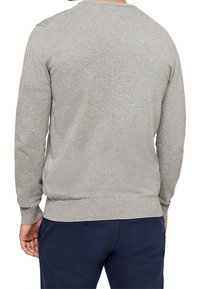 Pull gris en maille avec un col rond, des manches longues et un ourlet côtelé. Le tissu présente une texture douce et un design simple.