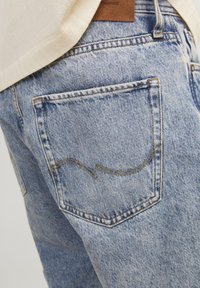 Világoskék farmernadrág, hátul egy jellegzetes ívelt varrásmintával rendelkező zsebből és a derékrészen elhelyezett barna bőrcímkéből áll.
