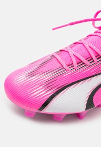 Scarpini da football con una tomaia rosa brillante, superficie testurizzata, accenti di design in bianco e nero e tacchetti traslucidi rosa. I lacci sono dello stesso rosa.