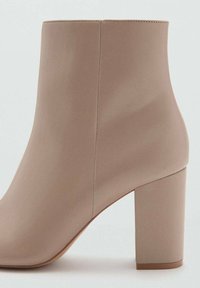Bottine beige avec une finition lisse, un bout carré et un talon bloc épais. Présente un design sans couture sans quincaillerie visible.