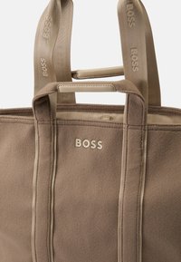 Brown fabric tote bag with light brown accents. Features large "BOSS" branding, two top handles, and reinforced stitching.