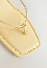 Geltoni plokšti sandalai su blizgiu paviršiumi, plonais dirželiais, su mazgu ir kvadratine pado forma, su matomais siuvimo detalėmis.