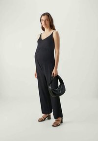 Black jumpsuit with a fitted bodice and wide legs, paired with a textured black handbag and strappy black heels. Smooth fabric, minimal design.