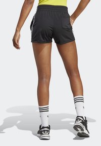 Pantaloni sportivi neri con una texture liscia, cintura elastica e strisce bianche sui lati. Indossati con scarpe nere e calzini bianchi a righe.