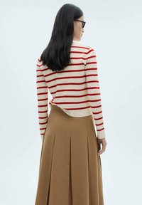 Pruhovaný svetr v krémové a červené barvě, s dlouhými rukávy a zkráceným střihem, spárovaný s béžovou sukní s vysokým pasem a sklady.