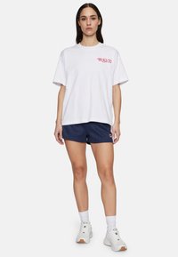 Valkoinen lyhythihainen t-paita, jossa on punainen "R.S.V.P." -painatus, yhdistetty tummansinisiin raidoitettuihin shortsihin, joissa on logotagi, ja valkoisilla lenkkareilla.