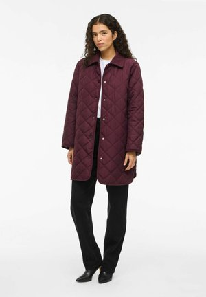Bordeaux gekleed gewatteerd jasje met een kraag, drukkers en lange mouwen. Gecombineerd met zwarte broek en puntige zwarte schoenen. Fluweelzachte textuur.