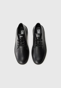 Zapatos de cuero negros con una textura suave, puntera redondeada, diseño de Cordones de dos ojales y un sutil logotipo en la plantilla.