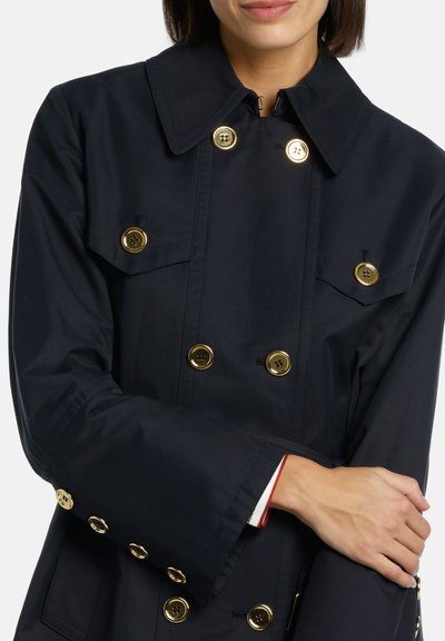 Jūras spēku dubultās krūšu žakete, izgatavota no gludas auduma, ar zeltītām pogām, divām krūšu kabatām un platu apkakli ar kontrastējošu iekšējo apdari.