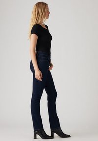 Top corto de mangas cortas ribeteado en negro, combinado con jeans de pierna recta azul oscuro que tienen bolsillos y una costura sutil, llevado con botas de tobillo de tacón negro.