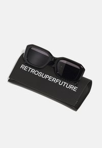 Black sunglasses with rectangular lenses, resting on a matte black case. The case features white text reading "RETROSUPERFUTURE."