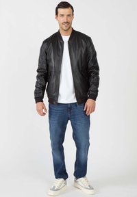 Zwarte leren bomberjack met een zachte textuur, geribbelde manchetten en kraag, gecombineerd met blauwe denim jeans en lichte sneakers.