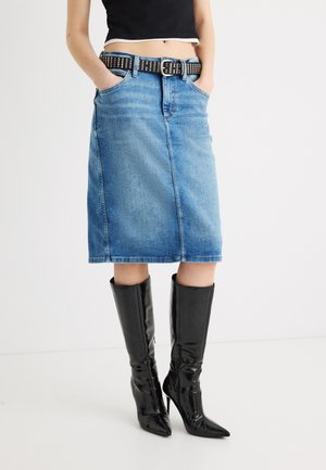 Ženska, oblečena v modro denim krilo, dolžine do kolen, z črnim pasom z zakovicami in črnimi škornji z visokimi petami in koničastimi prsti, ki segajo do kolen.