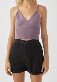 Camiseta de punto lavanda de corte corto con escote en V y textura acanalada, combinada con pantalones cortos de mezclilla negros de tiro alto con doblez en los dobladillos.