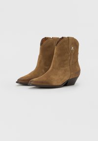 Bottes de cowboy en daim marron avec des orteils pointus, des coutures décoratives et un talon bas. Présente un emblème sur le côté pour un branding subtil.